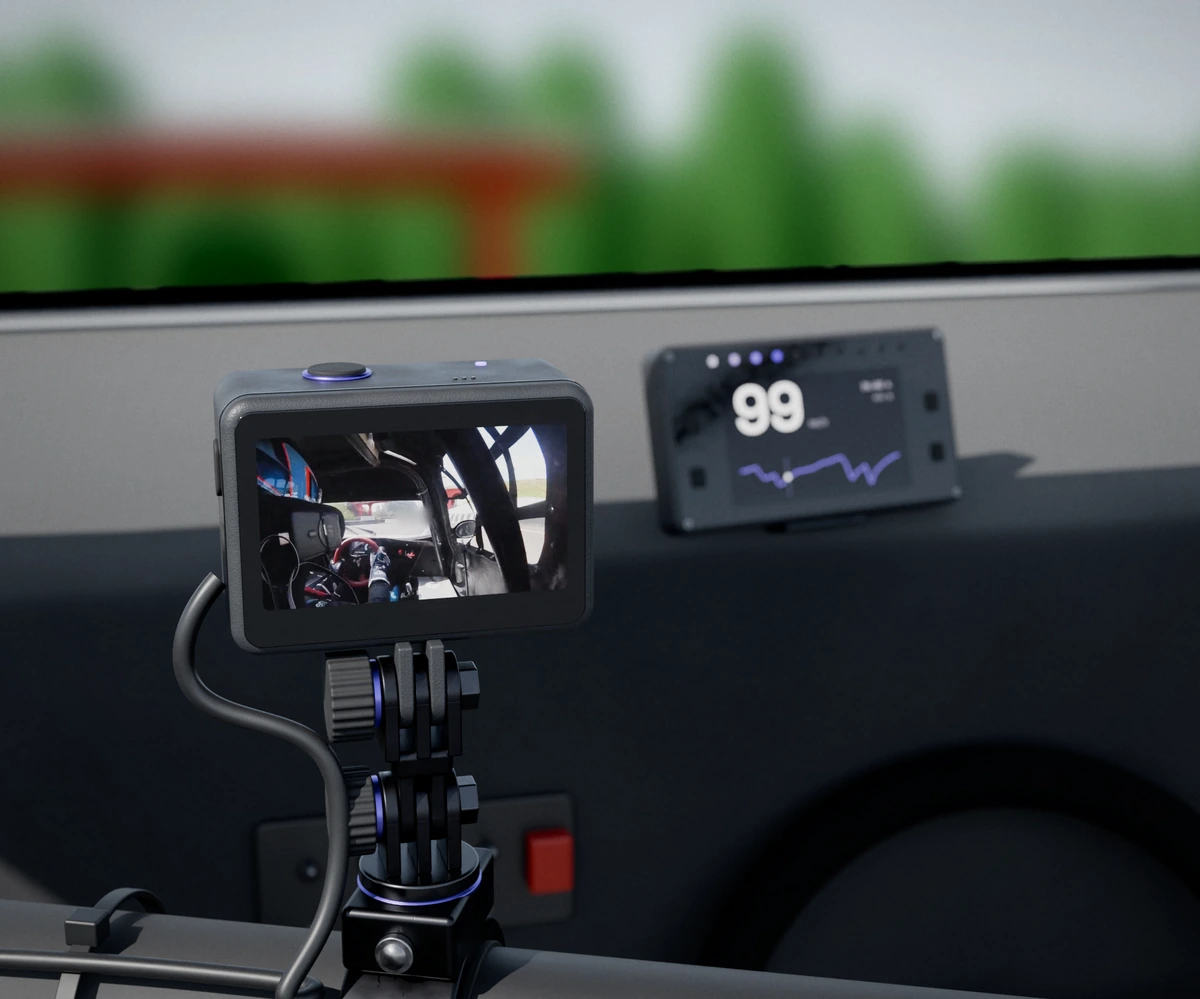 Dentro do carro, uma câmera de ação presa por braçadeira no santo-antônio mostra na tela o onboard do Vitor Genz no Velopark. Ao fundo, desfocado, o logger no painel marca 99 km/h com o traço de velocidade da volta.